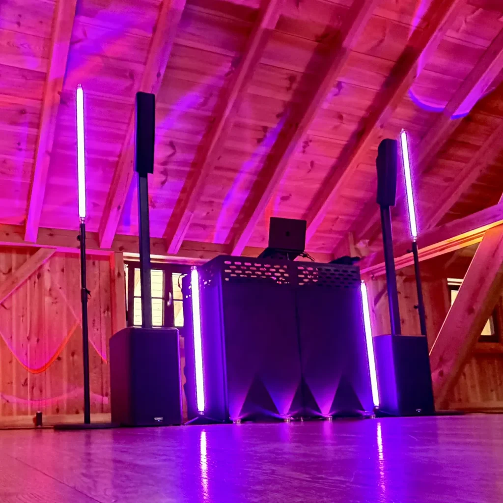 DJ-Pult mit QSC-Säulenlautsprechern und pinken APE-Labs-Lichtröhren in einer Holzscheune
