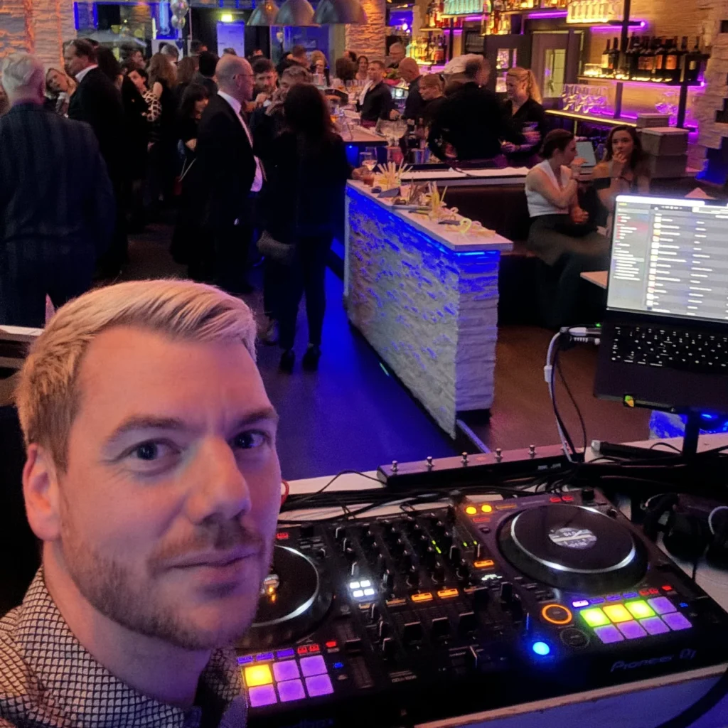 DJ New Inside am DJ-Pult bei einer Firmenfeier in München, dahinter Gäste an der beleuchteten Bar