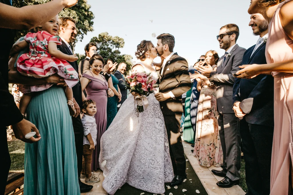 Hochzeit in München – Brautpaar küsst sich nach der Trauung, Gäste jubeln und werfen Blütenblätter