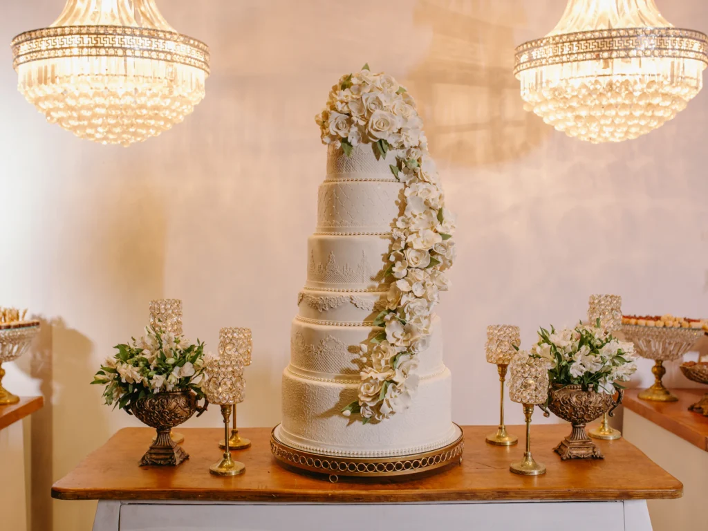 Weiße Hochzeitstorte mit Rosen auf einem Holztisch zwischen zwei Kronleuchtern